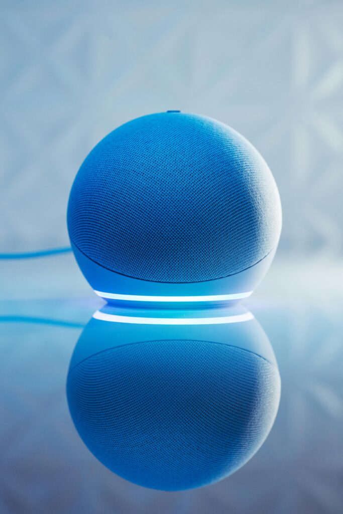 pexels-photo-14309813-14309813 A smart speaker with glowing blue LED lighting and its reflection on a surface.